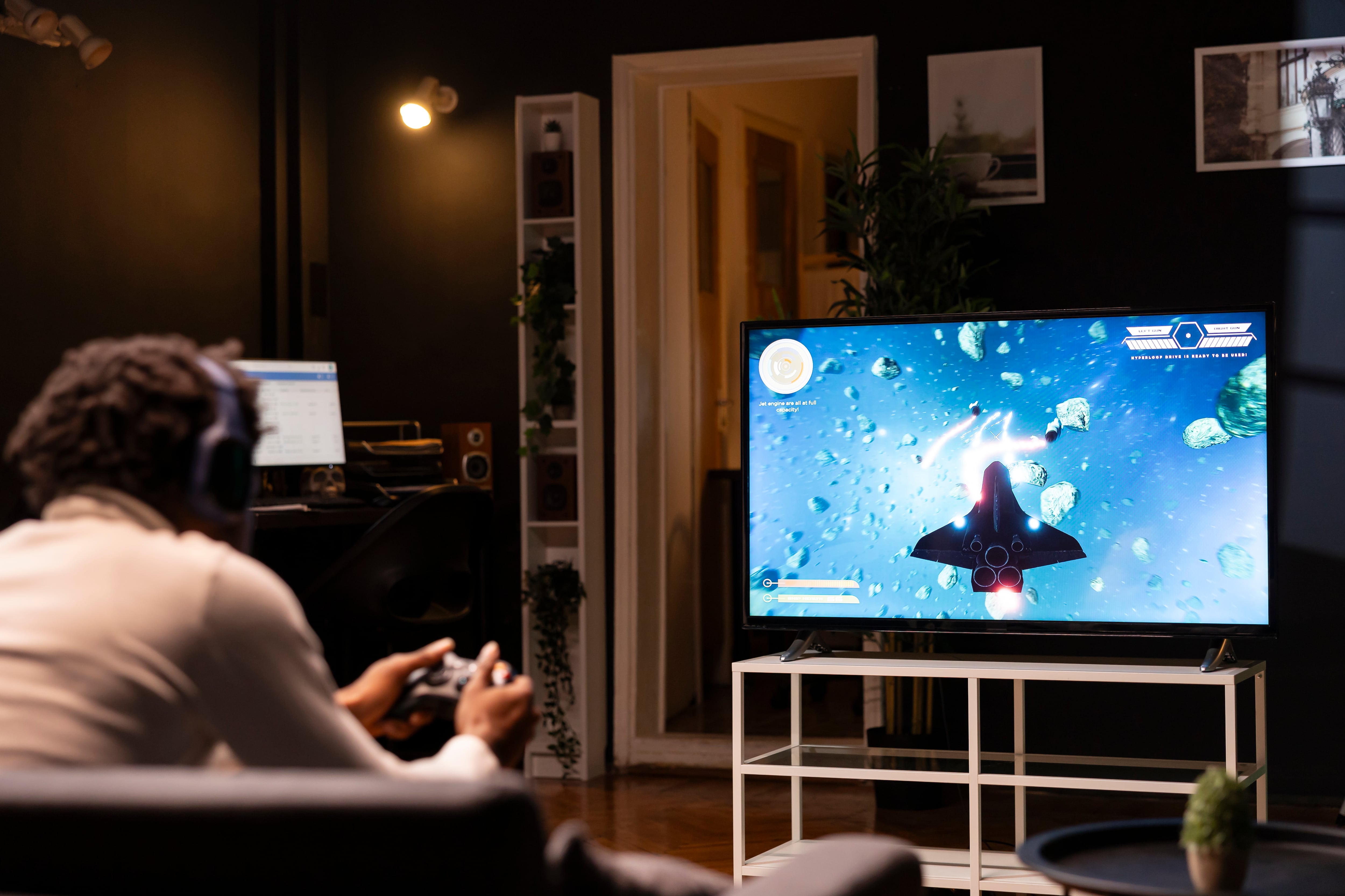 Gamer using controller and headphones to immerse himself in classic arcade videogame on smart TV, flying through space debris. African american ,an using high tech gaming console gamepad
