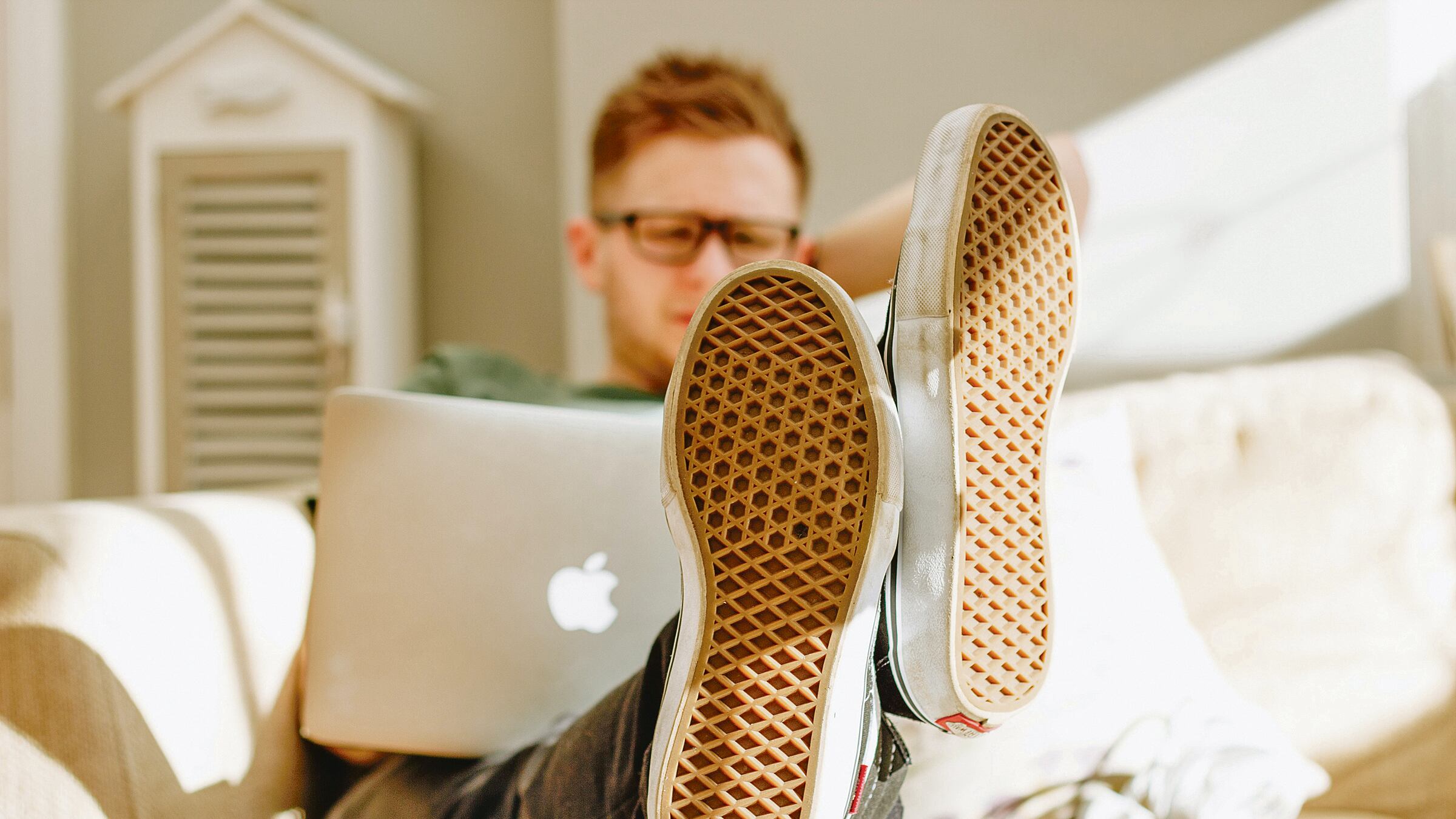 Joven sentado en un mueble con una computadora encima.